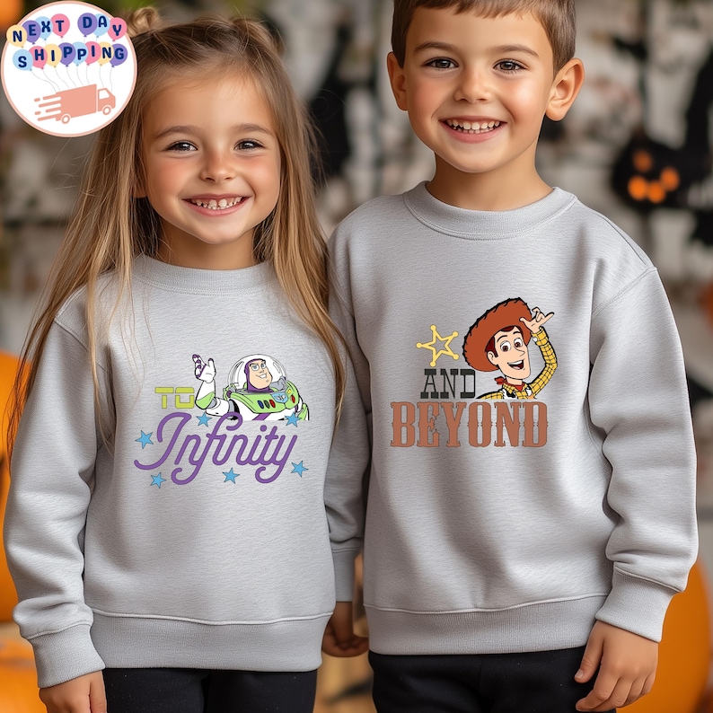 May include: Two children wearing light gray sweatshirts. One sweatshirt features Buzz Lightyear with the text "To Infinity" and stars. The other sweatshirt has Woody with the text "And Beyond" and a star. Both sweatshirts are long-sleeved.