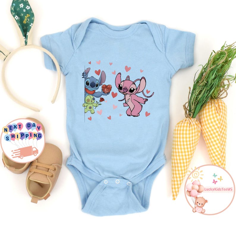 May include: A light blue baby onesie featuring a cartoon illustration of Stitch and Angel with hearts. Stitch is holding a heart-shaped box, and Angel is smiling. The onesie has a snap closure.