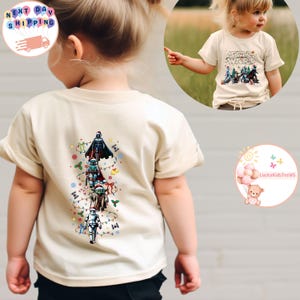 May include: A cream-coloured t-shirt with a Star Wars Christmas tree design. The tree is made up of characters including Darth Vader, Boba Fett, Yoda, and a Stormtrooper, all wearing Santa hats. The front of the shirt also displays the words "STAR WARS".