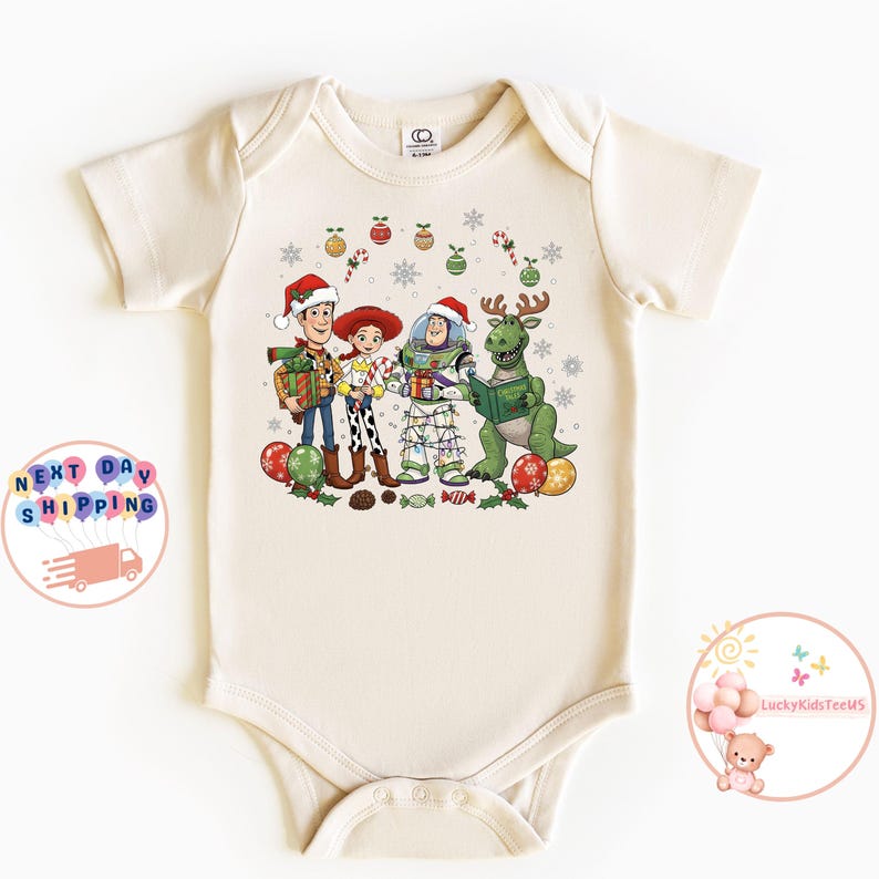 May include: A cream-coloured baby bodysuit with a festive graphic of Toy Story characters wearing Santa hats and surrounded by Christmas decorations. The design includes Woody, Jessie, Buzz Lightyear, and Rex, ideal for the holiday season.