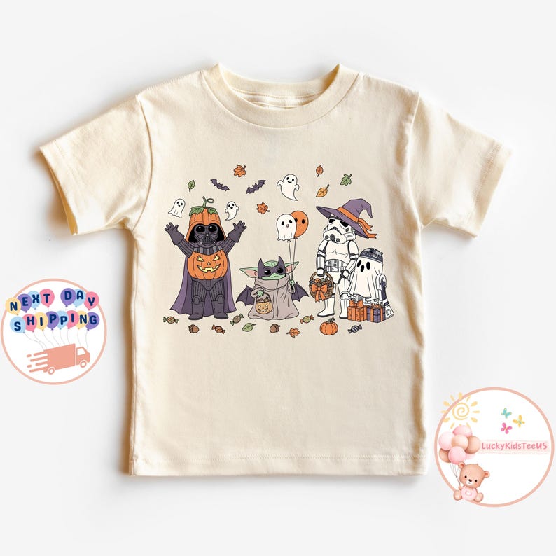 以下が含まれることがあります： ハロウィーンをテーマにしたグラフィックが特徴のクリーム色のTシャツ。デザインには、ダース・ベイダー、ストームトルーパー、ベビーヨーダに扮した漫画のキャラクター、カボチャ、幽霊、コウモリが含まれています。このシャツは柔らかい素材で作られています。