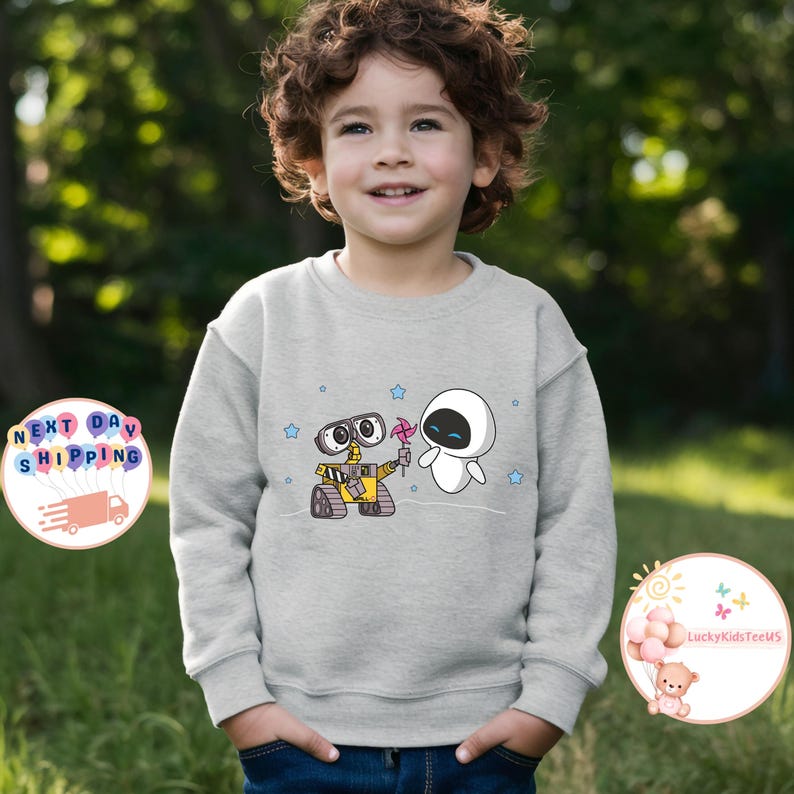 Puede incluir: Una sudadera gris con una imagen de dibujos animados de Wall-E y Eva de la pel&iacute;cula Wall-E. Los personajes sostienen una flor y est&aacute;n de pie sobre un fondo de estrellas.