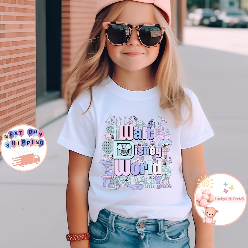 May include: A white t-shirt with a colorful graphic design featuring the text "Walt Disney World" and various iconic Disney attractions. The design is in pastel colors and includes a Mickey Mouse head.