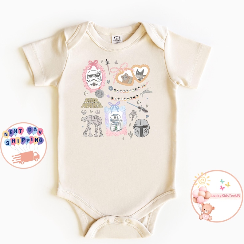 May include: A cream-coloured baby onesie with Star Wars illustrations. The design includes a Stormtrooper, R2-D2, and the Mandalorian helmet, along with the phrase "May the Force Be With You".