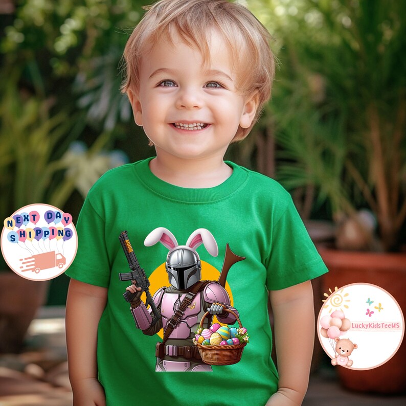 May include: A green t-shirt with a pink and white Easter bunny Mandalorian holding a basket of Easter eggs. The Mandalorian is wearing a helmet and has a blaster rifle in his left hand.