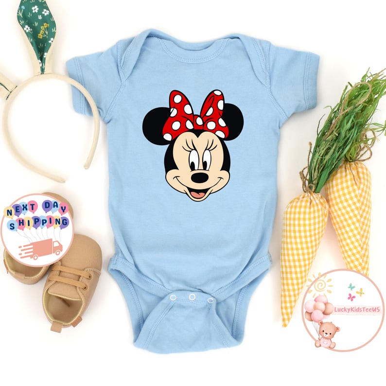 May include: A pale blue baby bodysuit with a Minnie Mouse design, including a red polka dot bow. The image includes baby shoes, a bunny ear headband, and decorative carrots. The text "Next Day Shipping" is also visible.