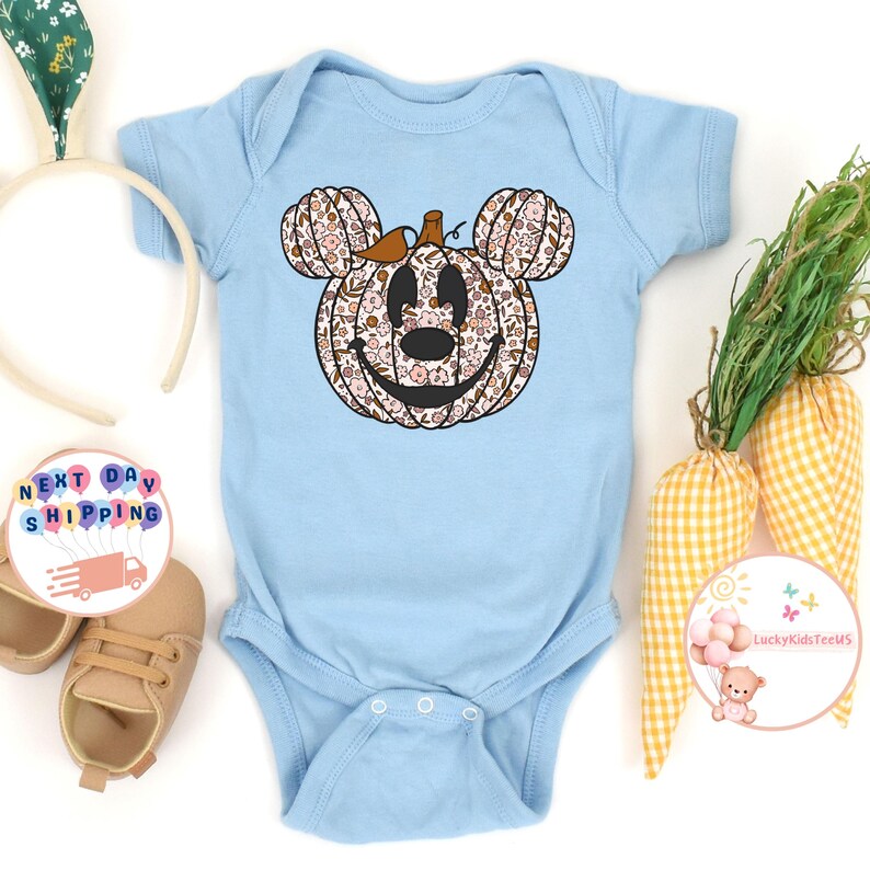 May include: A light blue baby onesie with a floral pumpkin design. The pumpkin is shaped like Mickey Mouse's head.