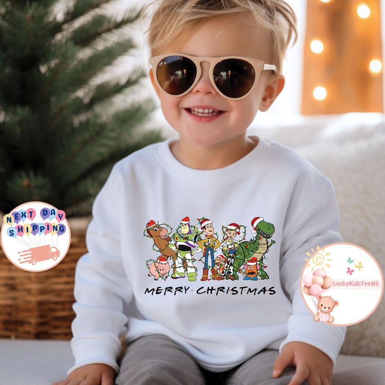 May include: White long-sleeved sweatshirt with a Christmas-themed design featuring the Toy Story characters wearing Santa hats and surrounded by Christmas lights. The text "Merry Christmas" is printed below the characters.