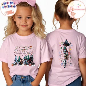 May include: Pink Star Wars t-shirts with a festive design. The front features characters in Santa hats and the Star Wars logo. The back shows a Christmas tree design with Star Wars characters. The shirts are worn by children.