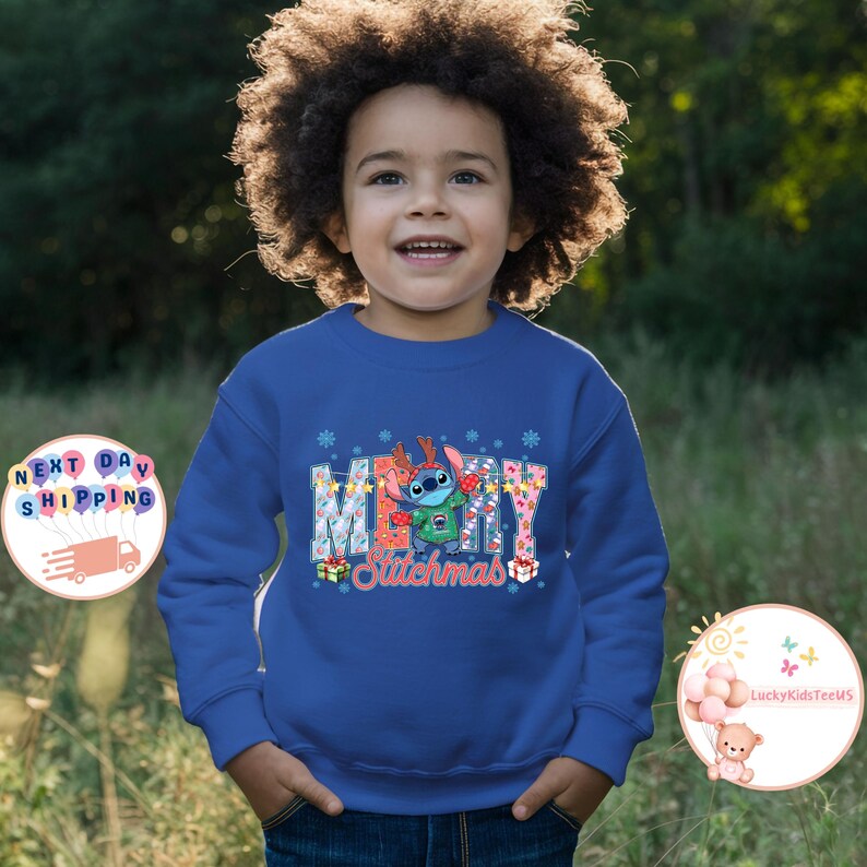 Puede incluir: Una sudadera azul con la palabra "MERRY" en una fuente colorida y estampada, con un personaje de dibujos animados de Stitch con un gorro de Pap&aacute; Noel. La palabra "Stitchmas" est&aacute; debajo. El ni&ntilde;o sonr&iacute;e.
