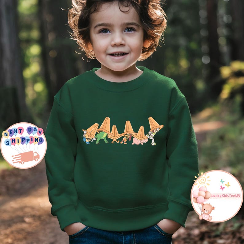 May include: A dark green sweatshirt featuring a cartoon design of characters wearing orange hats. The design is centered on the front of the sweatshirt. The sweatshirt is worn by a young child.
