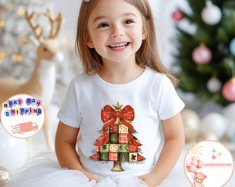 May include: A white t-shirt featuring a Christmas tree design. The tree is composed of patchwork squares in red, green, and gold, topped with a red bow and gold star. The shirt is worn by a young child.