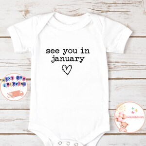 May include: White baby onesie with black text that reads "see you in january" with a hand-drawn heart below the text.