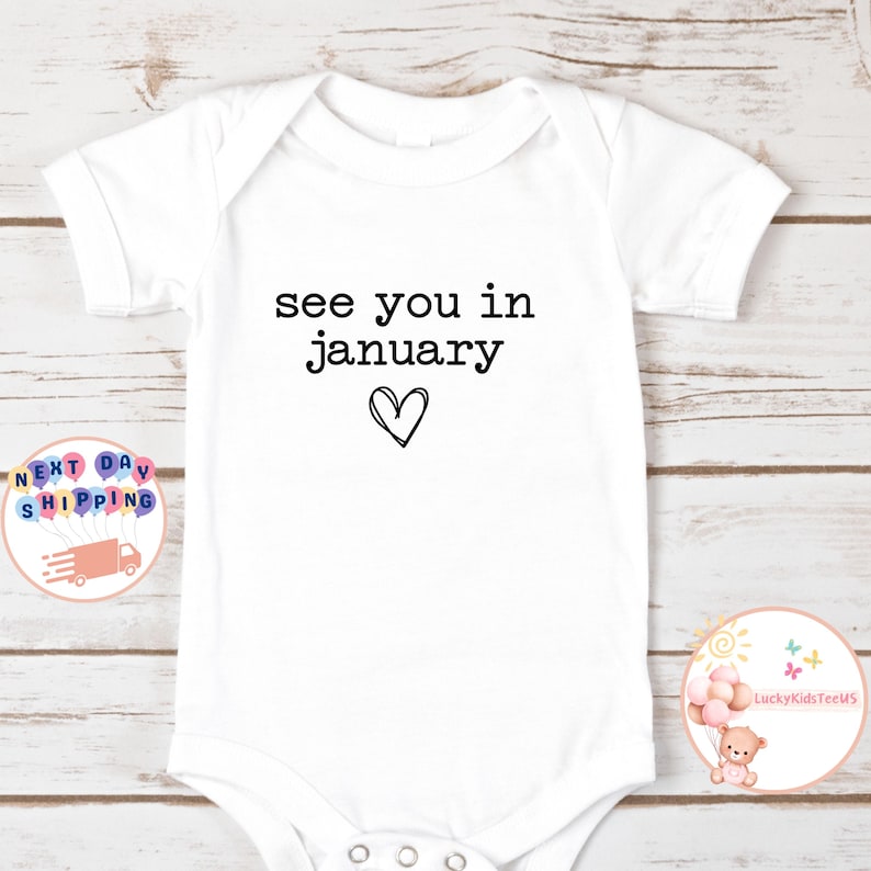 May include: White baby onesie with black text that reads "see you in january" with a hand-drawn heart below the text.