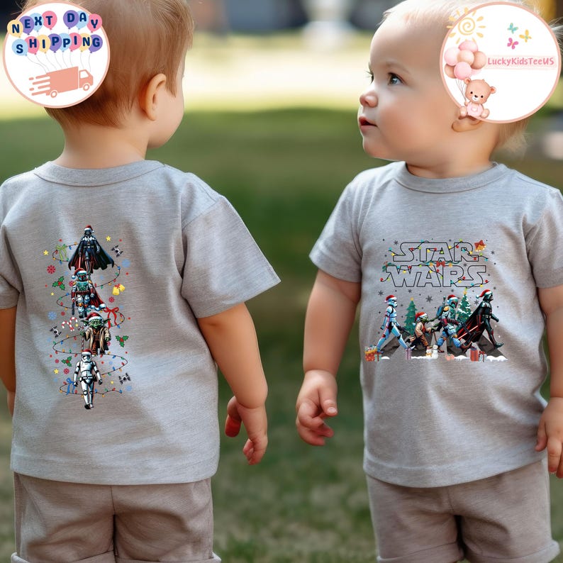May include: Two children wearing grey t-shirts. One shirt has a vertical design of Star Wars characters, the other displays the Star Wars logo with characters. Both shirts feature festive holiday elements.