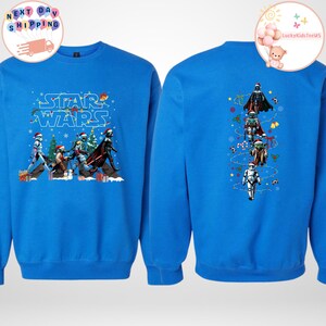 May include: A blue sweatshirt with a Star Wars Christmas design. The front has characters in Santa hats, with "Star Wars" in a festive font. The back shows a vertical arrangement of characters with Christmas decorations.