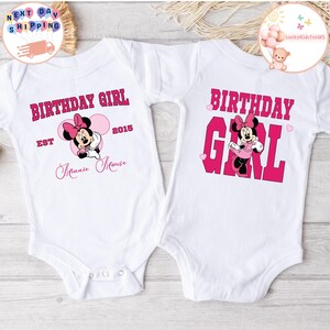May include: Two white onesies with pink and red graphics. One onesie says "Birthday Girl Est 2015 Minnie Mouse" with a pink Minnie Mouse graphic. The other onesie says "Birthday Girl" with a pink Minnie Mouse graphic.