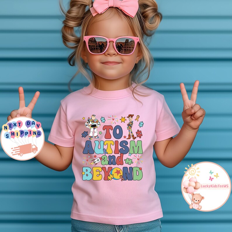 Puede incluir: Camiseta rosa con un gr&aacute;fico colorido de los personajes de Toy Story y el texto "TO AUTISM and BEYOND".