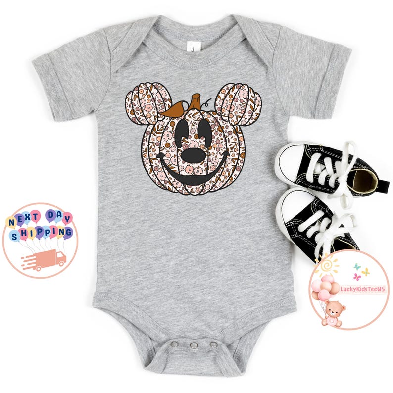 May include: A grey baby onesie with a floral pumpkin design in the shape of Mickey Mouse's head. The pumpkin has a brown stem and a smiling face.