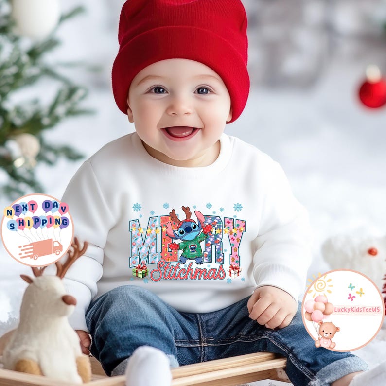 Puede incluir: Un beb&eacute; con una sudadera blanca con un gr&aacute;fico colorido de "Merry Stitchmas". El gr&aacute;fico presenta al personaje Stitch con un su&eacute;ter navide&ntilde;o y cuernos de reno. El beb&eacute; tambi&eacute;n lleva un gorro rojo y vaqueros azules.