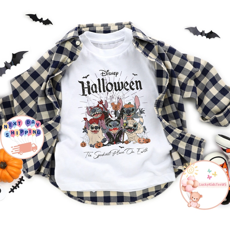 May include: White t-shirt with a Disney Halloween graphic featuring Stitch and friends in Halloween costumes. The shirt is layered under a blue and black plaid flannel shirt. Decorative bats and a pumpkin are also present.