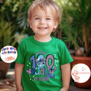 May include: A green t-shirt with a blue Stitch character from Disney's Lilo & Stitch. The shirt says "Happy 100th Day of School" with a purple and pink design.