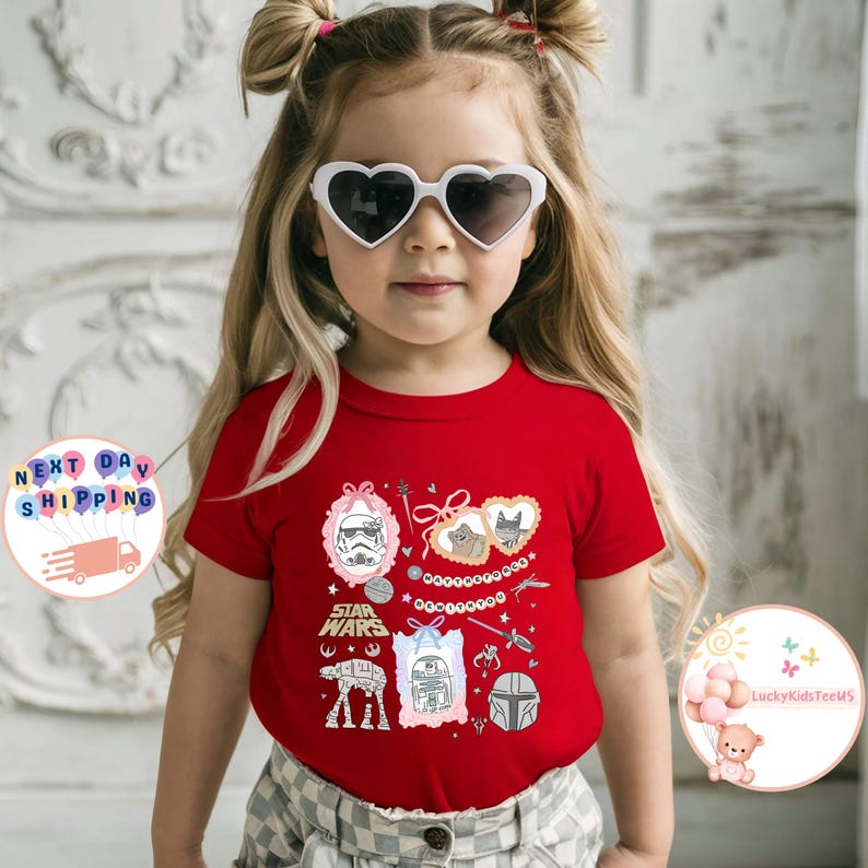 May include: A child wearing heart-shaped sunglasses and a red t-shirt. The t-shirt displays various Star Wars themed illustrations, including a Stormtrooper, AT-AT, R2-D2, and a Mandalorian helmet, alongside the Star Wars logo.