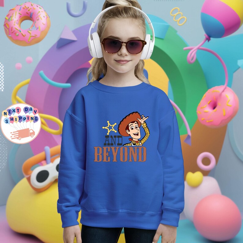 May include: A blue sweatshirt featuring a cartoon image of Woody from Toy Story, with the text "AND BEYOND". The sweatshirt is worn by a person wearing sunglasses and headphones. The background includes colorful shapes and donuts.