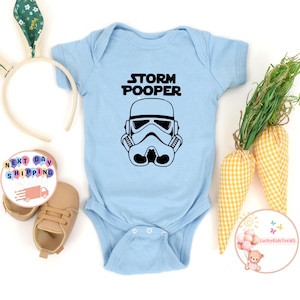 May include: Light blue baby onesie with a black and white illustration of a Star Wars Stormtrooper helmet and the text "STORM POOPER".