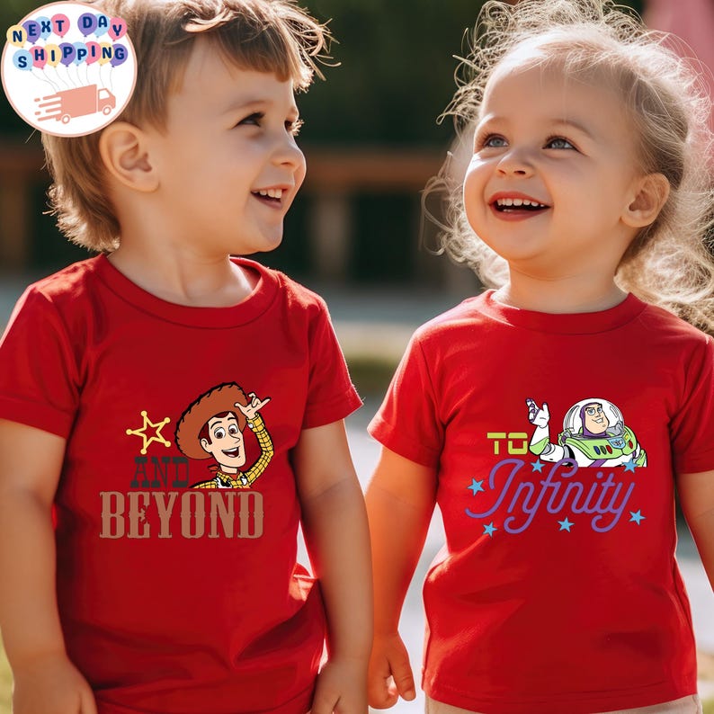 May include: Two children wearing red t-shirts with cartoon graphics. One shirt features Woody from Toy Story with the text "AND BEYOND". The other shirt has Buzz Lightyear and the phrase "TO Infinity".