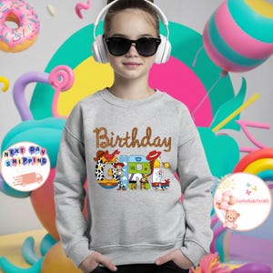 Op de afbeelding: Grijs sweatshirt met een afbeelding van Toy Story-personages die "Birthday Girl" spellen.
