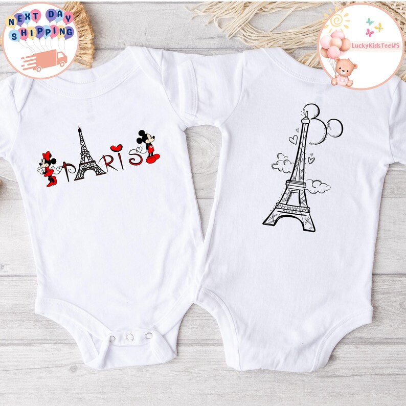 May include: Two white baby onesies with a black and white Eiffel Tower design. One onesie has the text "PARIS" with a red heart and Mickey Mouse characters.