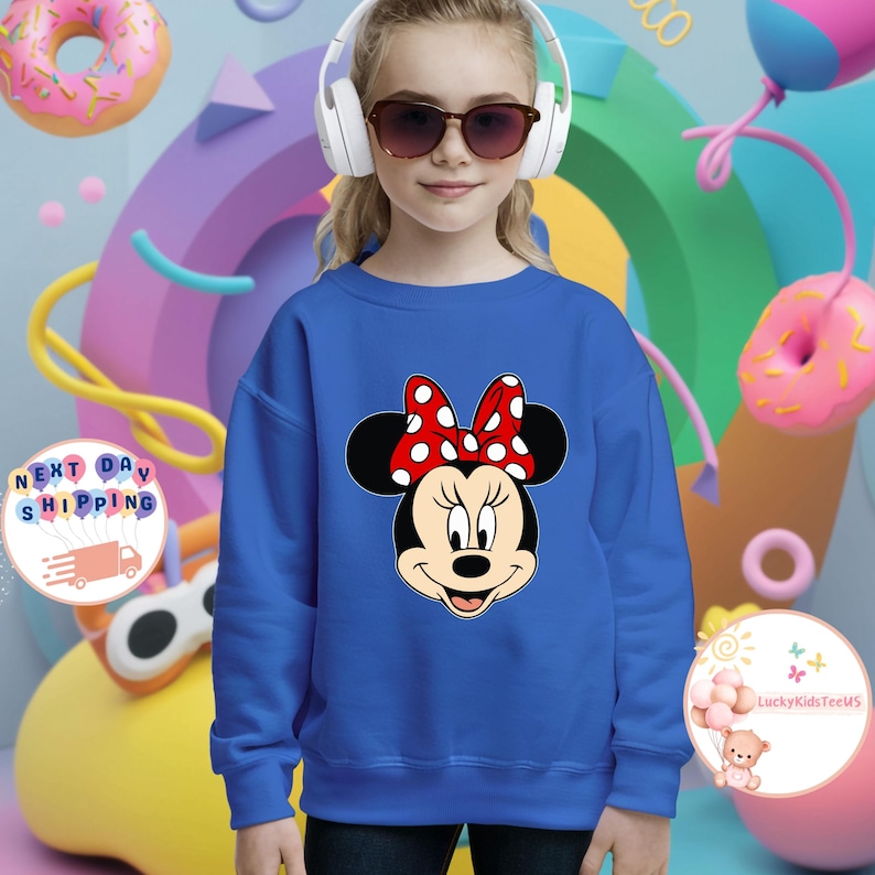 May include: A blue sweatshirt with a Minnie Mouse design, featuring a red polka dot bow. The image shows a young person wearing the sweatshirt, headphones, and sunglasses. The background includes colourful shapes and donuts.
