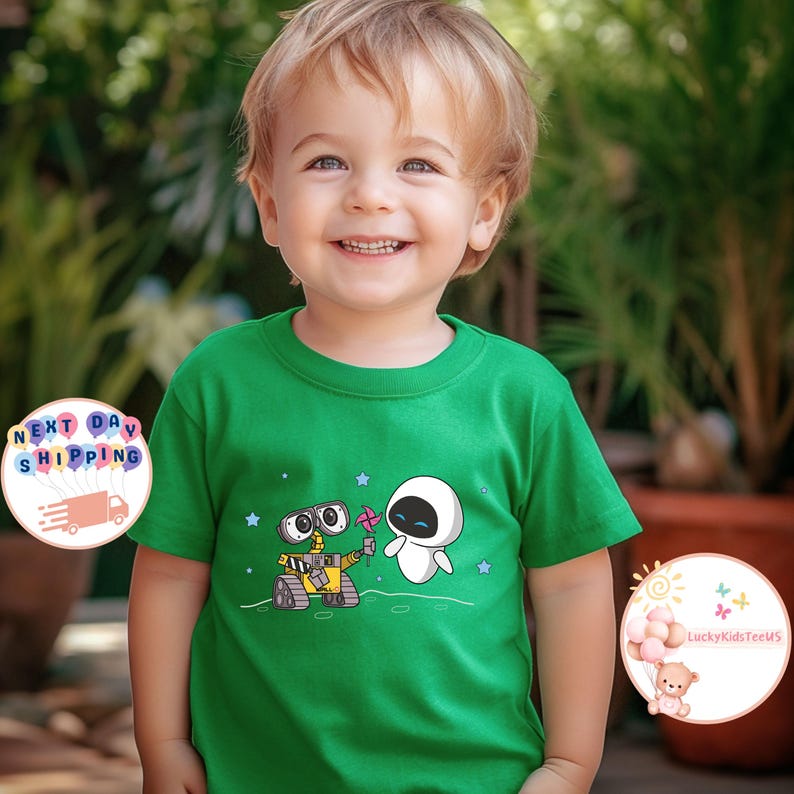 Puede incluir: Una camiseta verde para ni&ntilde;os peque&ntilde;os con una imagen de dibujos animados de Wall-E y Eve de la pel&iacute;cula Wall-E. La camiseta tiene un fondo blanco con estrellas y una luna gris.