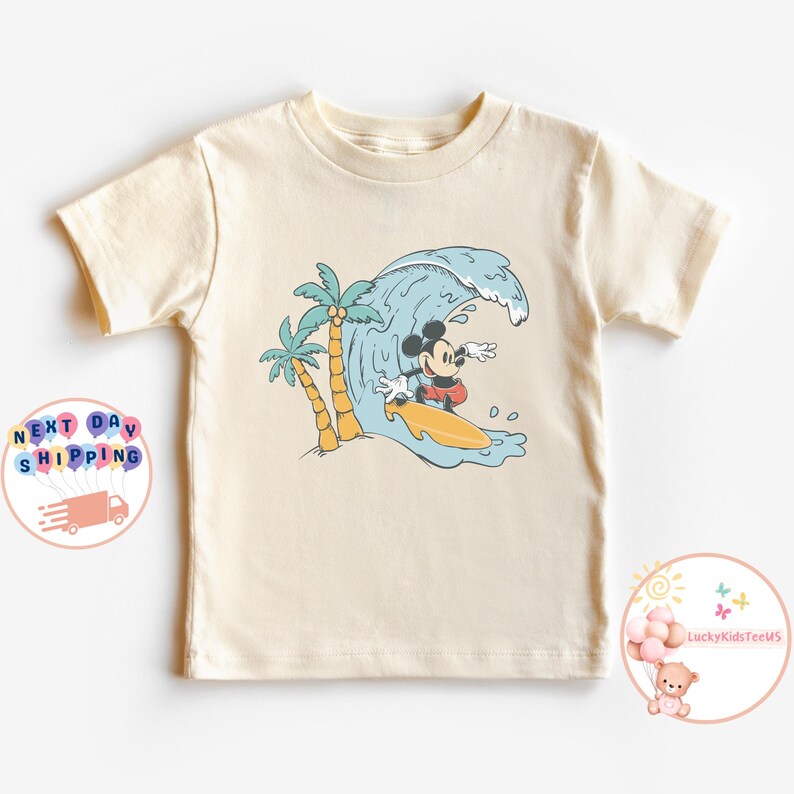 Puede incluir: Una camiseta de color crema con un gr&aacute;fico de Mickey Mouse surfeando en una ola con palmeras en el fondo.