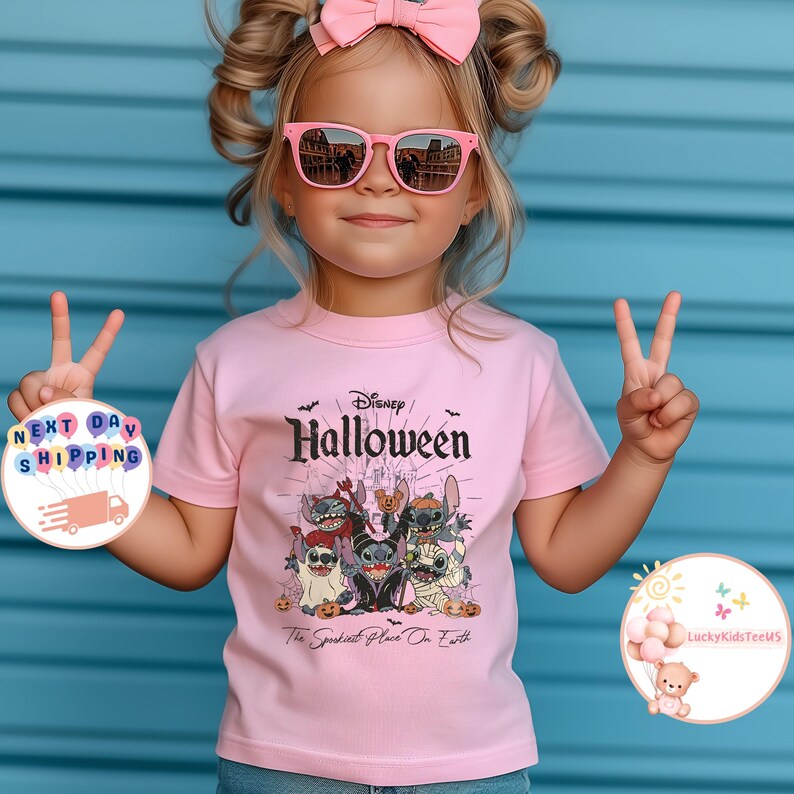 May include: A young child wearing a pink t-shirt with a Disney Halloween graphic. The shirt features various cartoon characters and the text "Halloween" and "The Spookiest Place On Earth". The child is also wearing pink sunglasses and a pink bow.