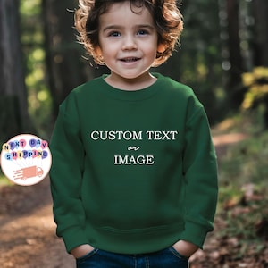 May include: A dark green sweatshirt with the text "CUSTOM TEXT or IMAGE" in white. The sweatshirt is worn by a young child. The image also includes a graphic with the words "NEXT DAY SHIPPING".
