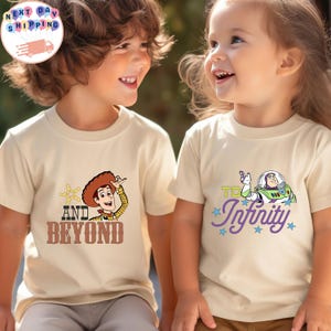 May include: Two children wearing beige t-shirts. One shirt features Woody with the text "AND BEYOND". The other shirt has Buzz Lightyear with the text "TO Infinity". Both shirts have colorful graphics and star accents.