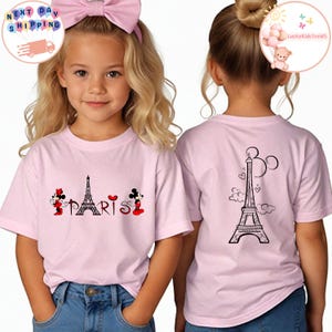 May include: Two pink t-shirts with a Paris theme. One shirt features Mickey and Minnie Mouse with the Eiffel Tower and the word "PARIS". The other shirt features the Eiffel Tower with Mickey Mouse ears.