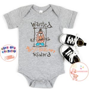 May include: A grey baby grow with a drawing of a cartoon potato head character with the text "Wanted &pound;50 Billion Reward".