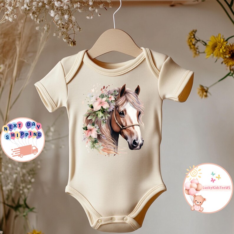 May include: A cream-colored baby onesie featuring a watercolor illustration of a horse's head adorned with flowers. The horse has a brown mane and a white blaze. The onesie is hanging on a wooden hanger.