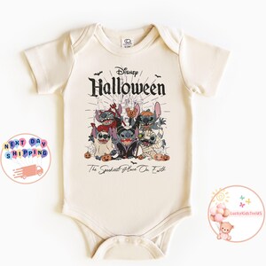 May include: Cream-colored baby bodysuit featuring a Halloween-themed graphic. The design includes the word "Disney" above "Halloween" and a group of cartoon characters in costumes. The text "The Spookiest Place On Earth" is below the graphic.
