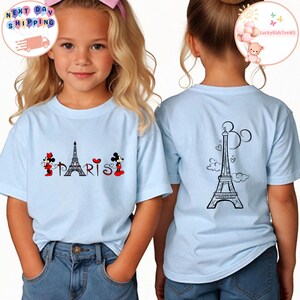 May include: Light blue t-shirt with a graphic of Mickey Mouse and Minnie Mouse in front of the Eiffel Tower with the word "PARIS" underneath. The back of the shirt has a graphic of the Eiffel Tower with Mickey Mouse ears.