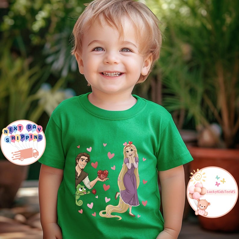 May include: A green t-shirt featuring a cartoon illustration of a princess and a prince, surrounded by pink hearts. The prince is holding a heart-shaped gift. The shirt has a round neck and short sleeves. The text "LuckyKidsTeeUS" is visible.