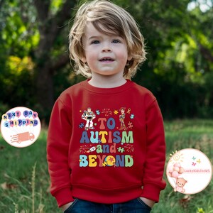 Puede incluir: Sudadera roja de manga larga con un gr&aacute;fico colorido de personajes de Toy Story y el texto "To Autism and Beyond".