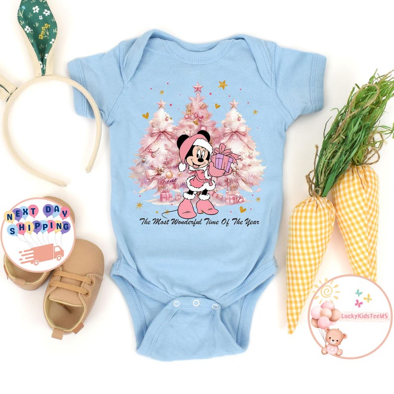 May include: A light blue baby onesie featuring a Minnie Mouse graphic holding a gift in front of pink Christmas trees. The text "The Most Wonderful Time Of The Year" is printed below the graphic. The onesie has short sleeves.