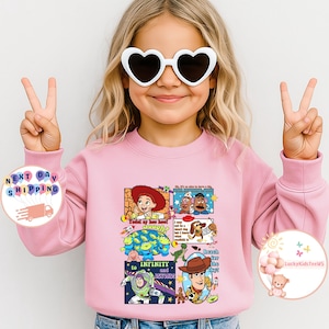 Puede incluir: Una sudadera rosa claro con un gr&aacute;fico colorido de personajes de Toy Story. El dise&ntilde;o incluye im&aacute;genes de Woody, Buzz Lightyear y otros personajes, junto con las frases "To Infinity and Beyond" y "Reach for the Sky!"