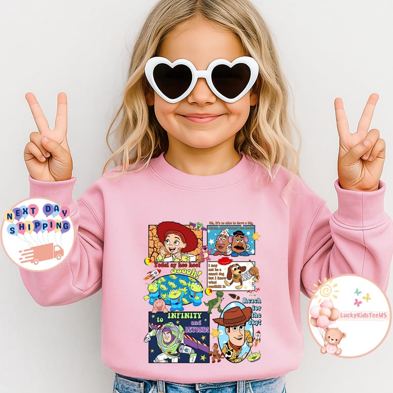Puede incluir: Una sudadera rosa claro con un gr&aacute;fico colorido de personajes de Toy Story. El dise&ntilde;o incluye im&aacute;genes de Woody, Buzz Lightyear y otros personajes, junto con las frases "To Infinity and Beyond" y "Reach for the Sky!"