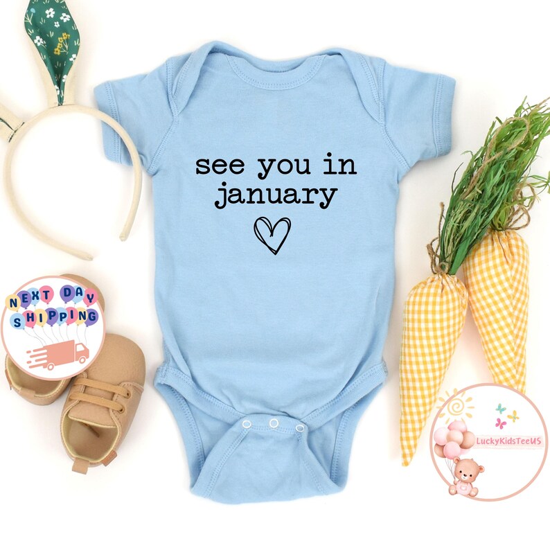 May include: A light blue baby onesie with the text "see you in january" and a small heart.