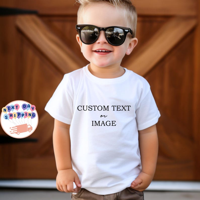 May include: A white t-shirt with the text "CUSTOM TEXT or IMAGE" in black. The child is wearing black sunglasses. The background is a wooden door.